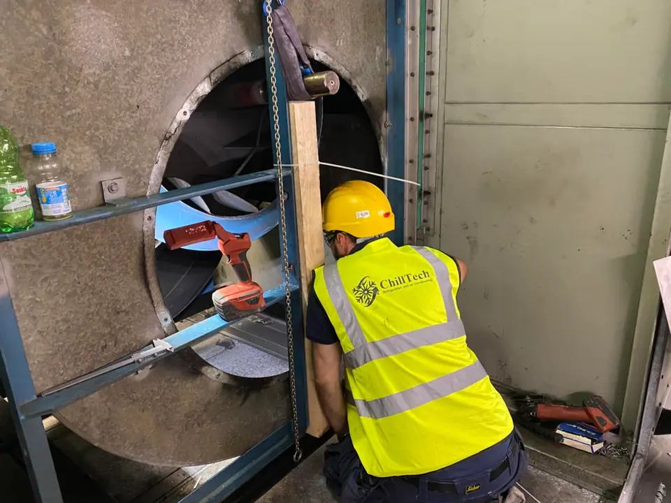 Engineer in hi-vis working inside a large air-handling duct